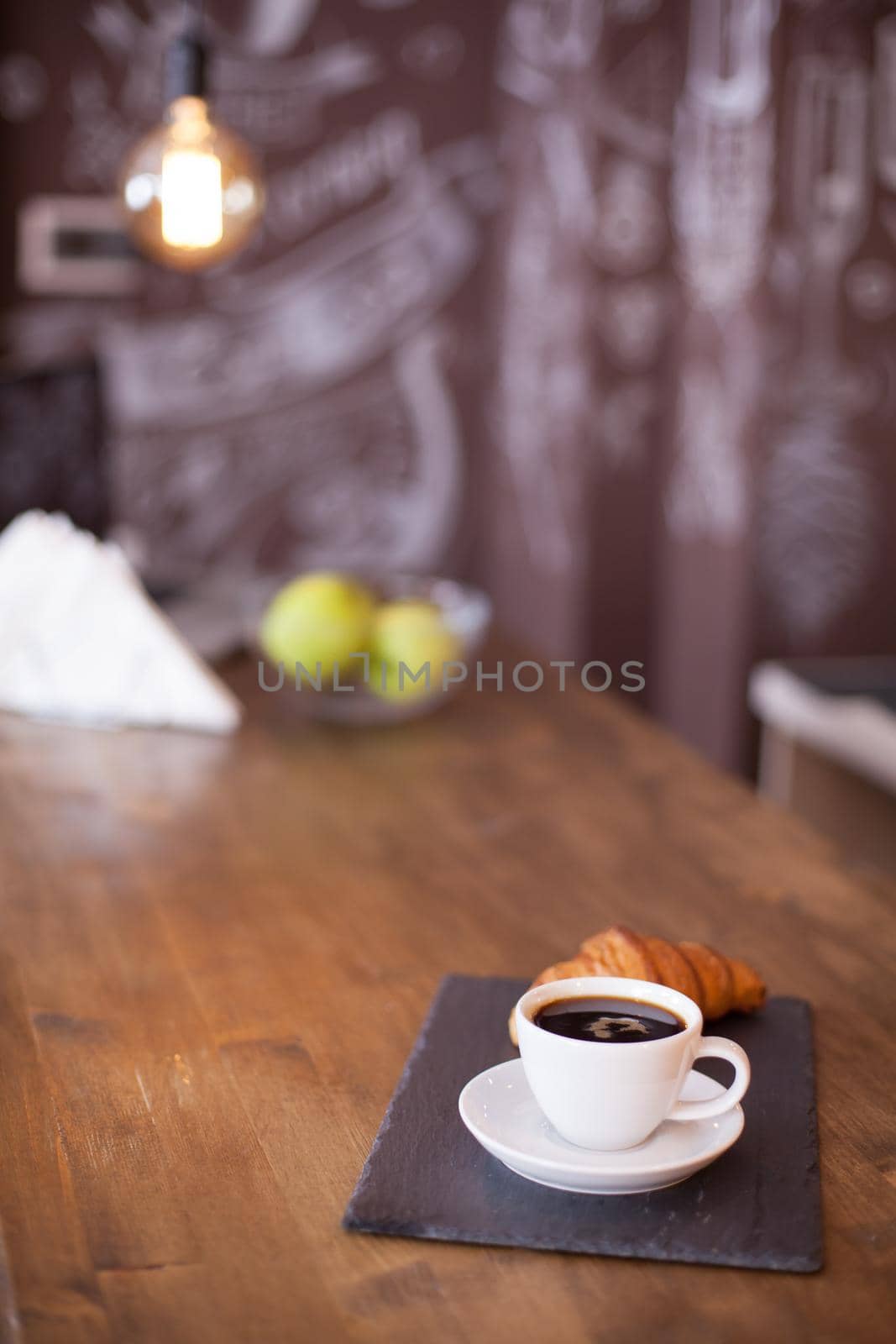Black coffee served with delicious croissant with blurred drawing in the background. Hand drawing. Coffee shop design.