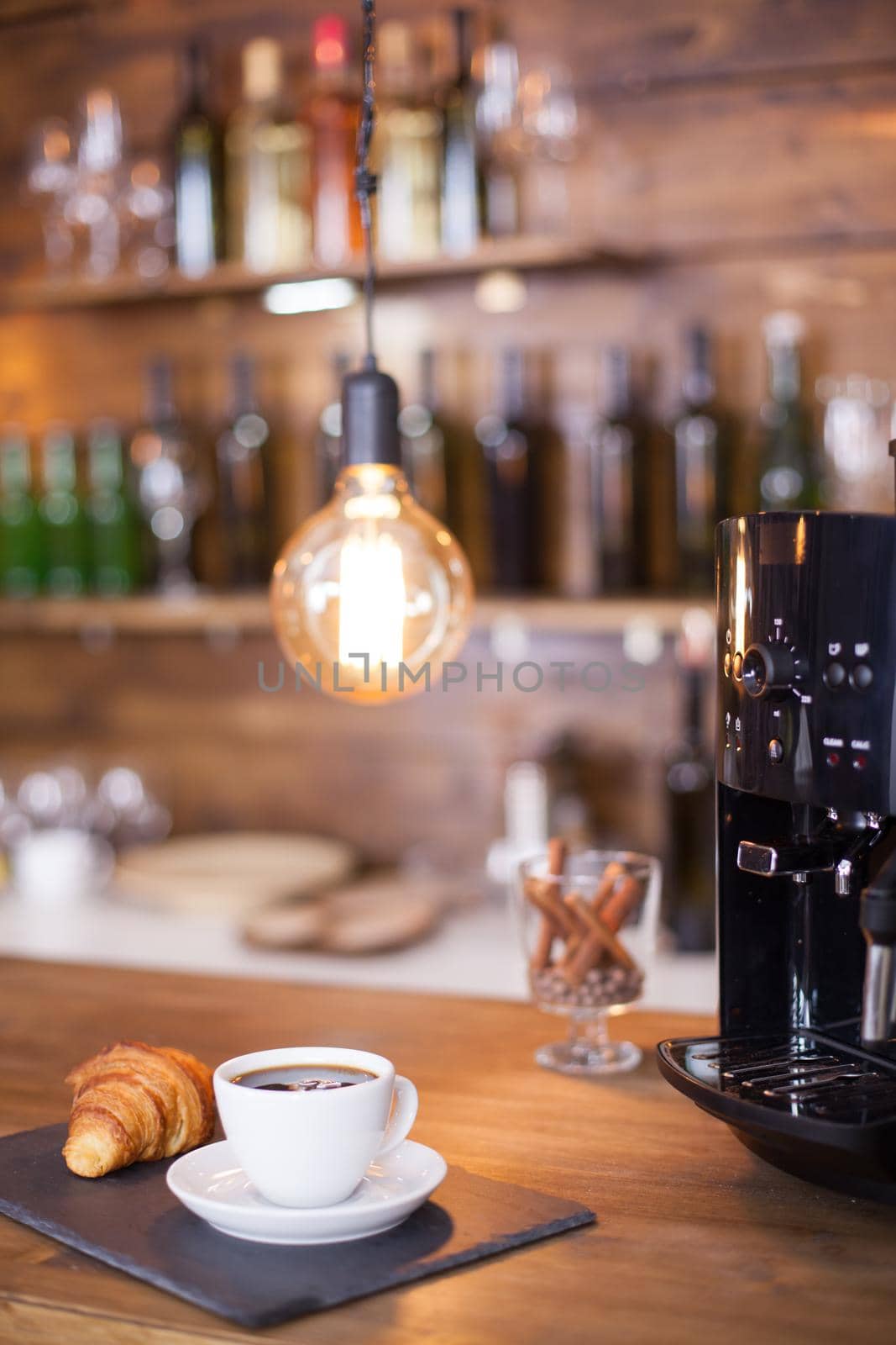 Modern coffee machine next to a cup of esoresso coffee on wooden counter bar. Vintage coffee shop. Tasty coffee.