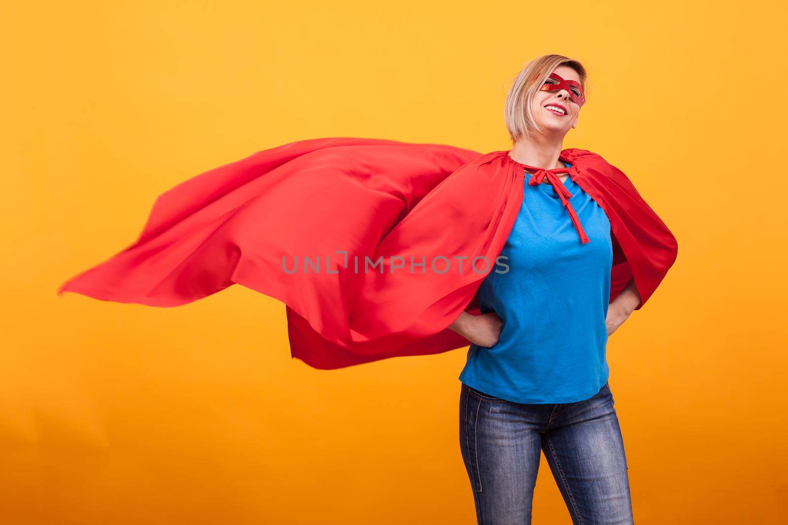 Young and beautiful blonde woman dressed like superheroine with red cape in the air. Red mask. Woman super powers. Red mask.