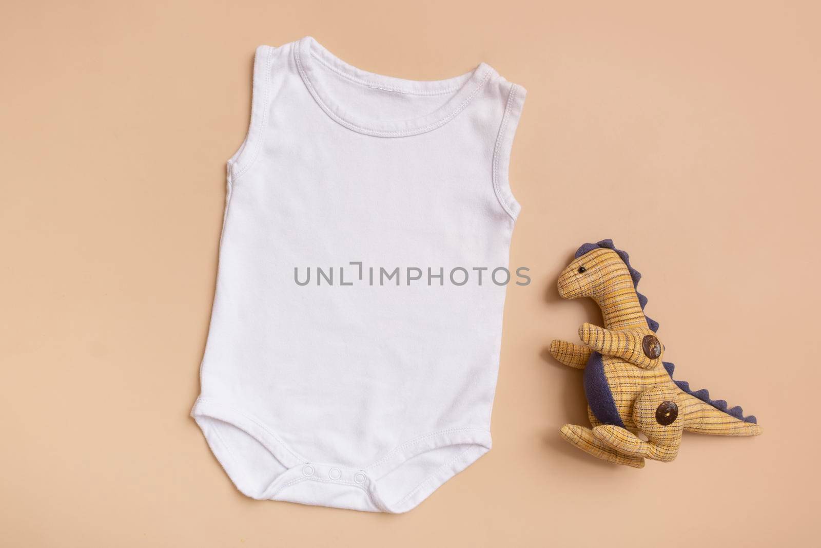 White baby bodysuit top view. Mock up for logo, text or design on beige background. Flat lay with dinosaur. High quality photo
