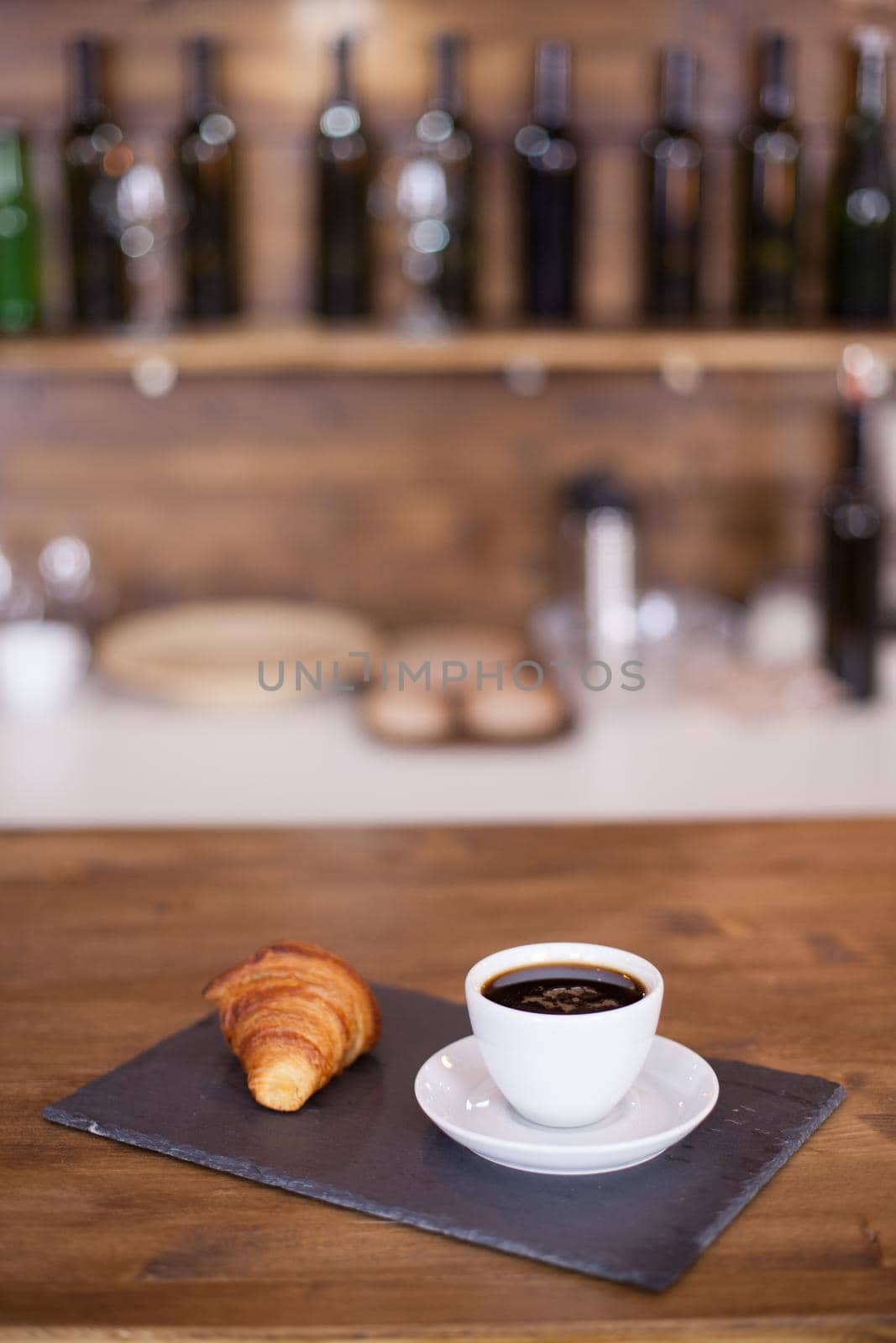 Black coffee served on the bar counter with blurred background. Tasty croissant.