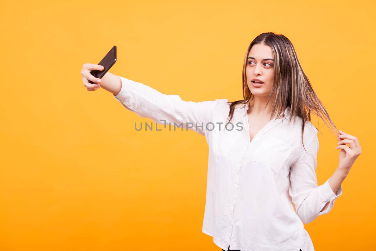 Portrait of pretty girl wearing a white shirt making a selfie over yellow background. Sexy attitude