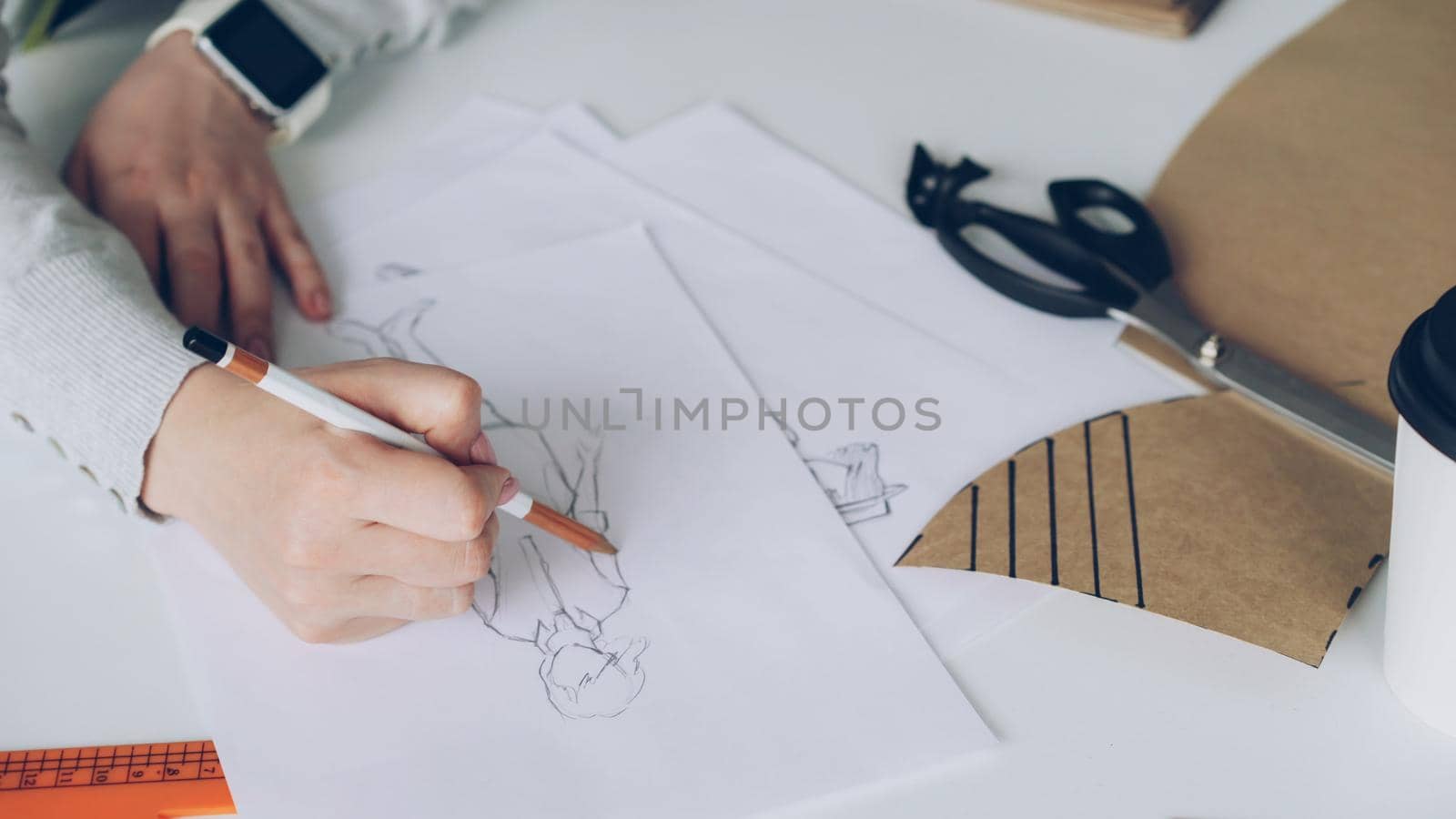 Close-up of fashion designer is drawing lines on clothing sketch. Woman is busy and concentrated on work.