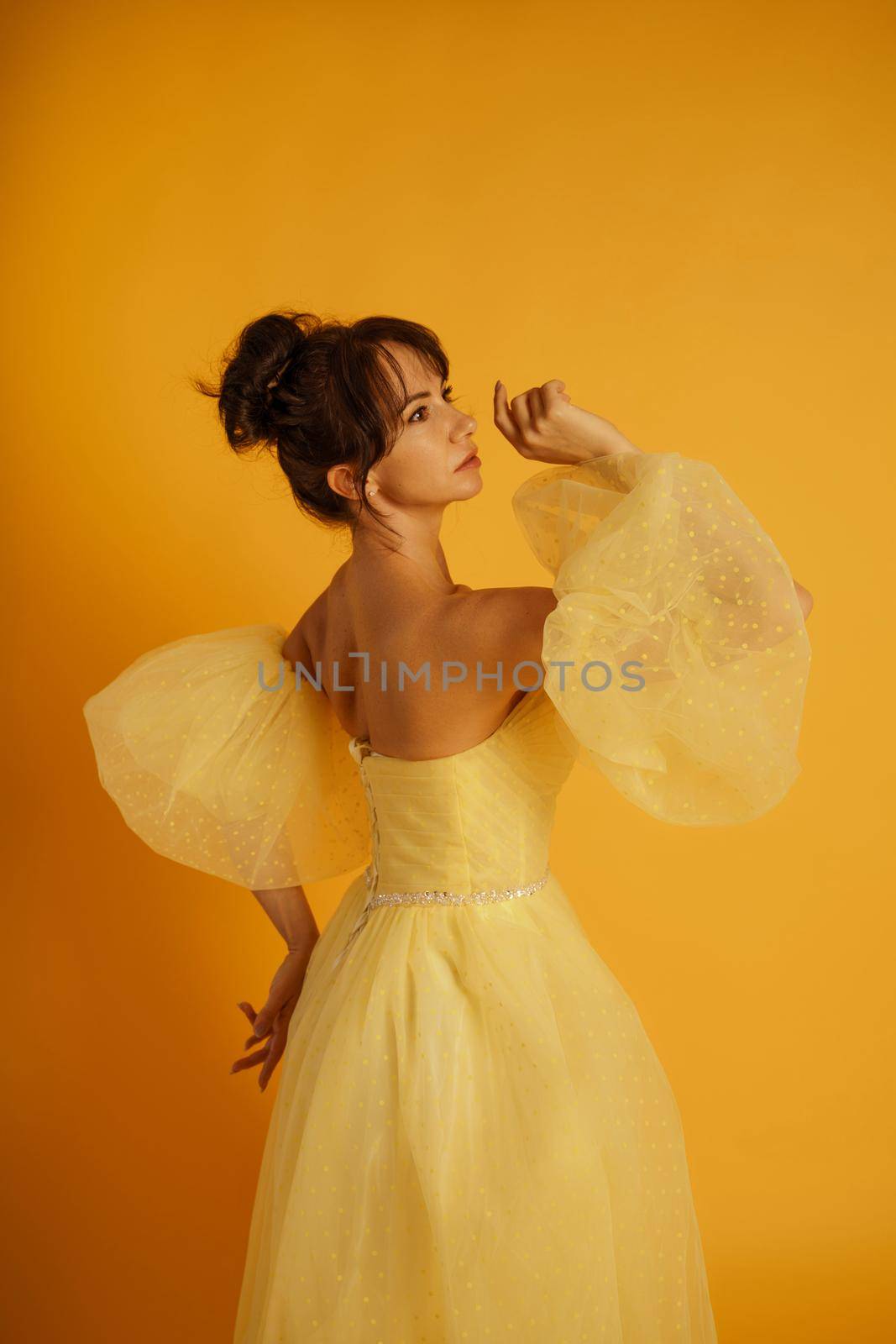 Portrait of a beautiful middle-aged woman in a yellow dress, her hair pulled up against a yellow background.