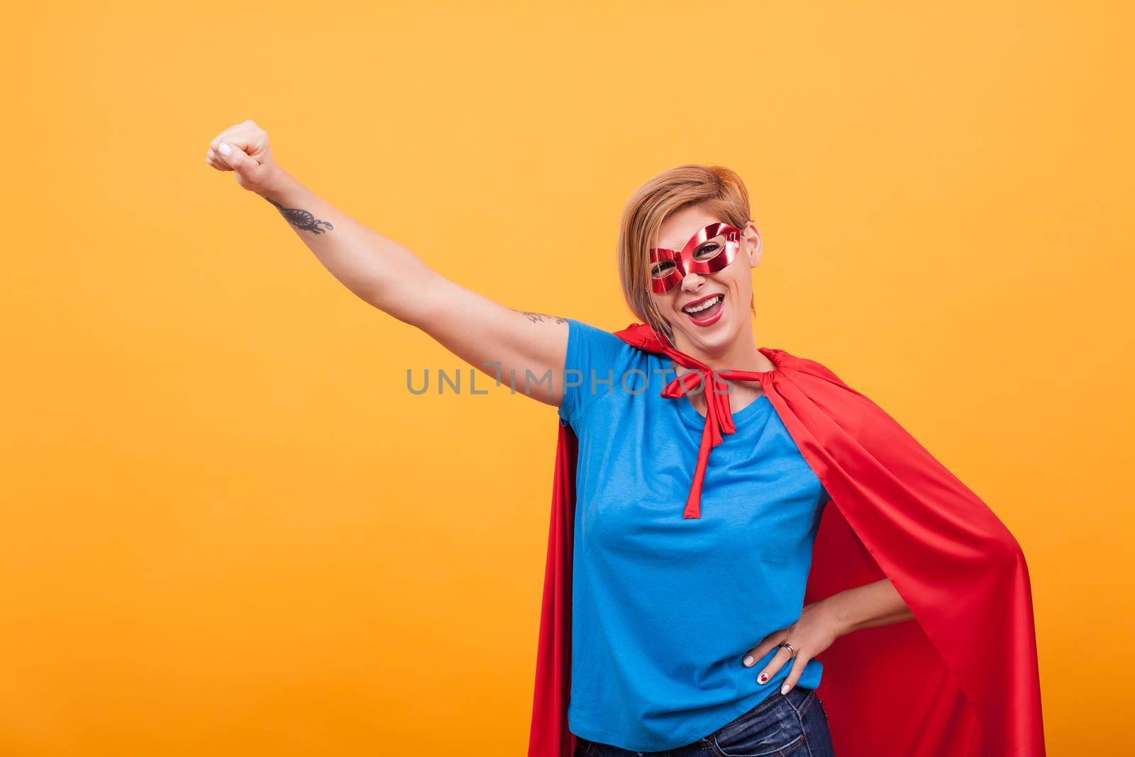 Young woman dresed like superheros flying off to save the world over yellow background by DCStudio