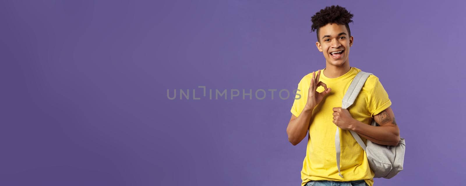 Back to school, university concept. Portrait of young handsome hipster guy, student with backpack assure test be good, show okay sign, chill and relax no worried, all ok, purple background.