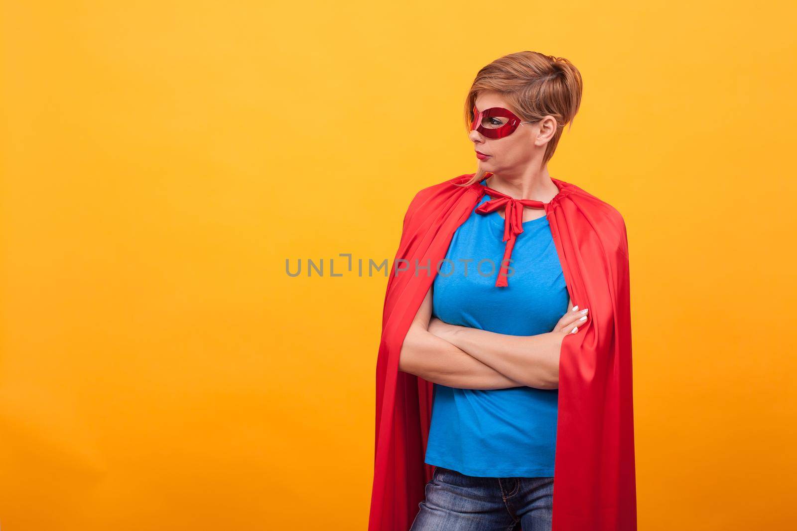 Woman dressed like superhores standing proudly and looking away over yellow background by DCStudio