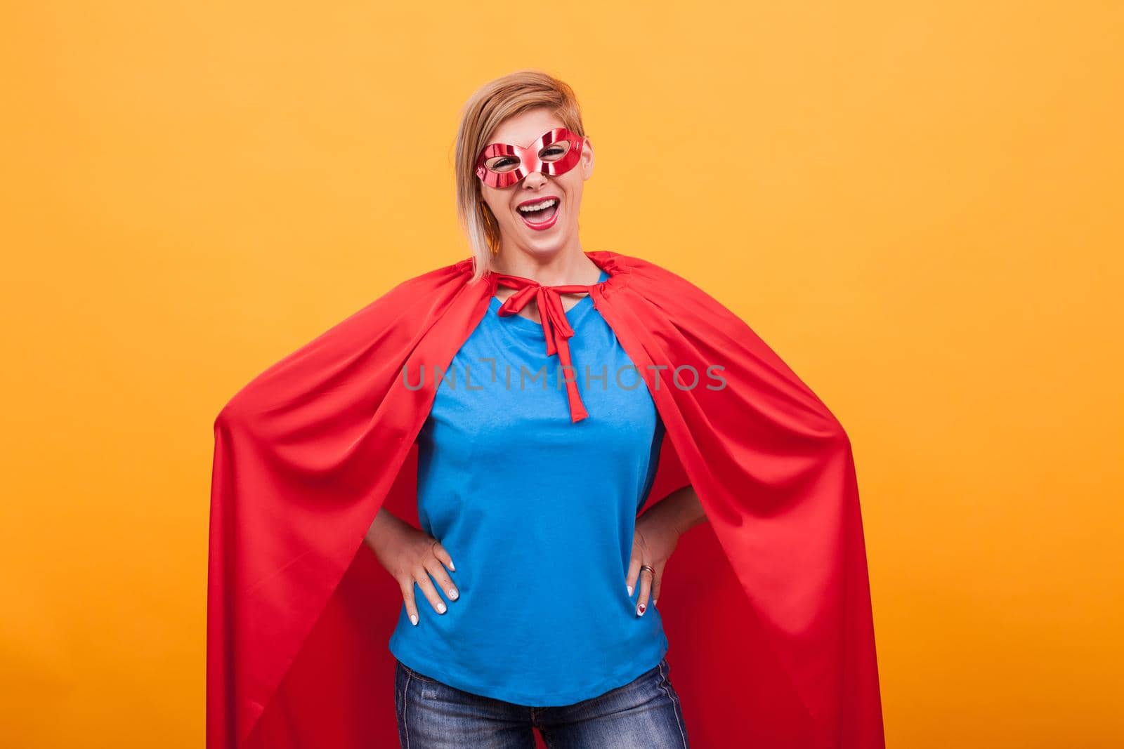 Mother dressed like superheros laughing at the camera over yellow background by DCStudio