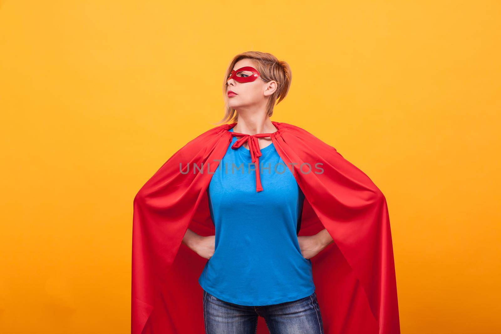 Young woman in superheros costume standing proudly over yellow background. Super powers. Red cape. red mask.