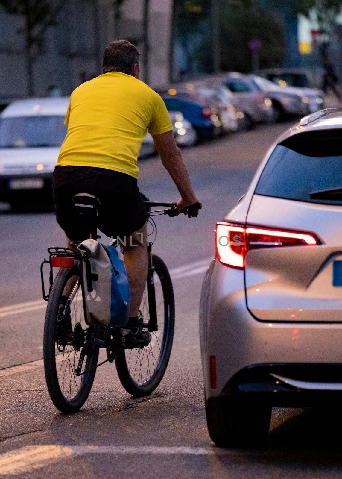 Cyclist overtaking car in a a road with low light. Rider in a risky or danger situation. rear view