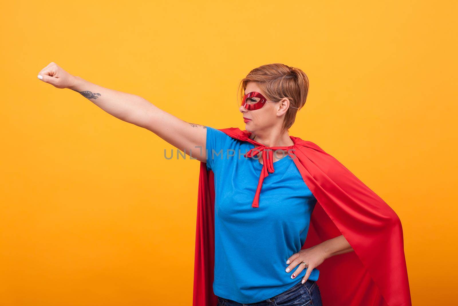 Young woman dresed like superheros flying off to save the world over yellow background. Woman super powers.