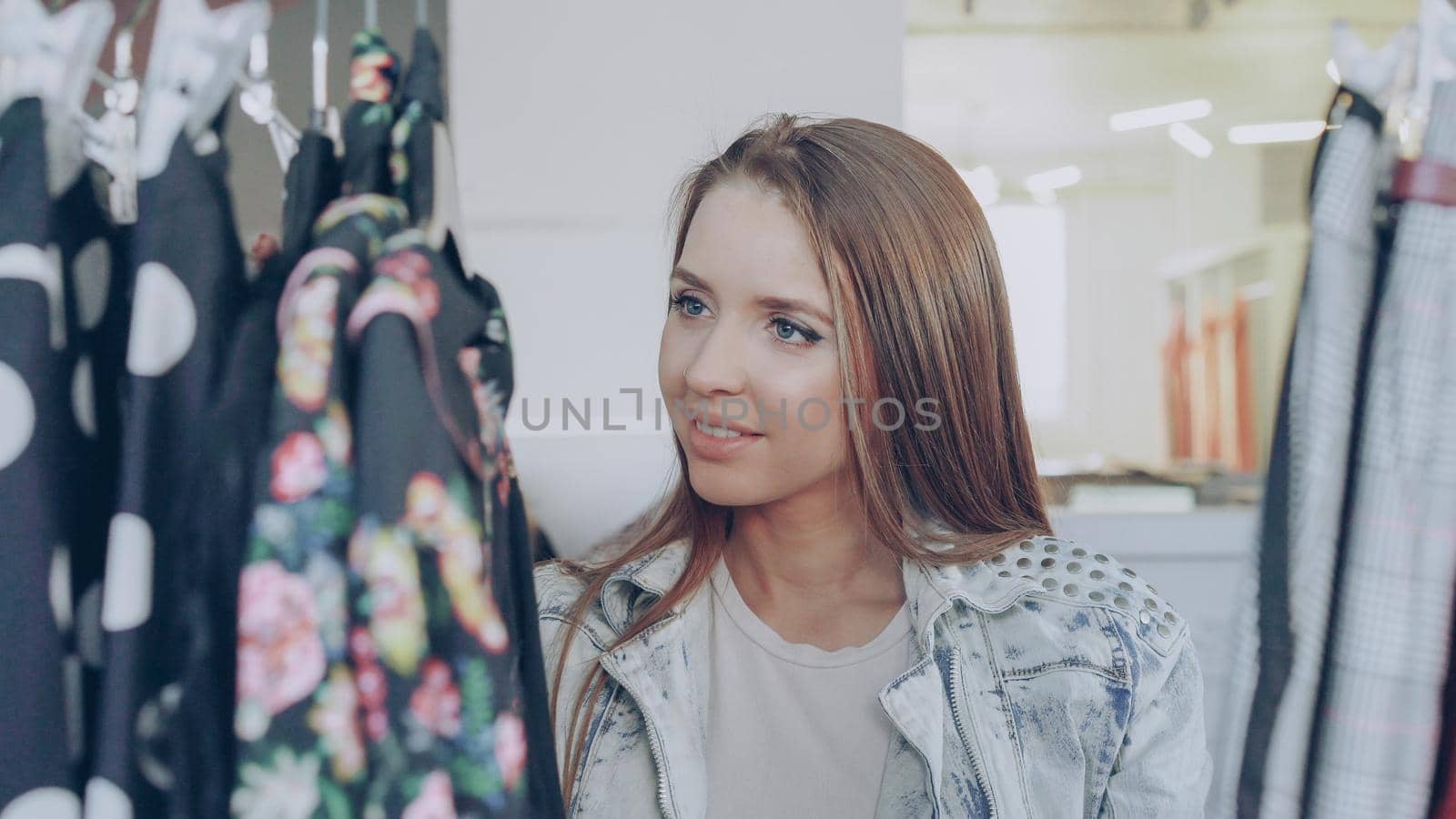 Close-up shot of young lady shopping for clothes, going through colourful garments on rails, touching and moving them. Trendy women's clothing in the foreground.