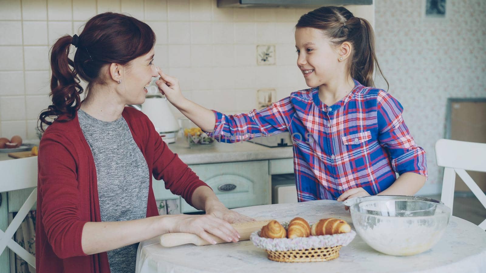 Happy mother and cute daughter have fun smearing nose each other with flour while cooking together in the kitchen on holidays. Family, food, home and people concept by silverkblack