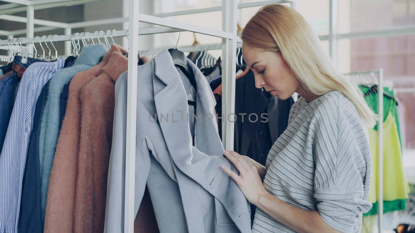 Close-up shot of young woman choosing coat in shop. First she is examining fabric , looking at buttons, underlinimg and belt, then taking coat off hanger and going away with it by silverkblack