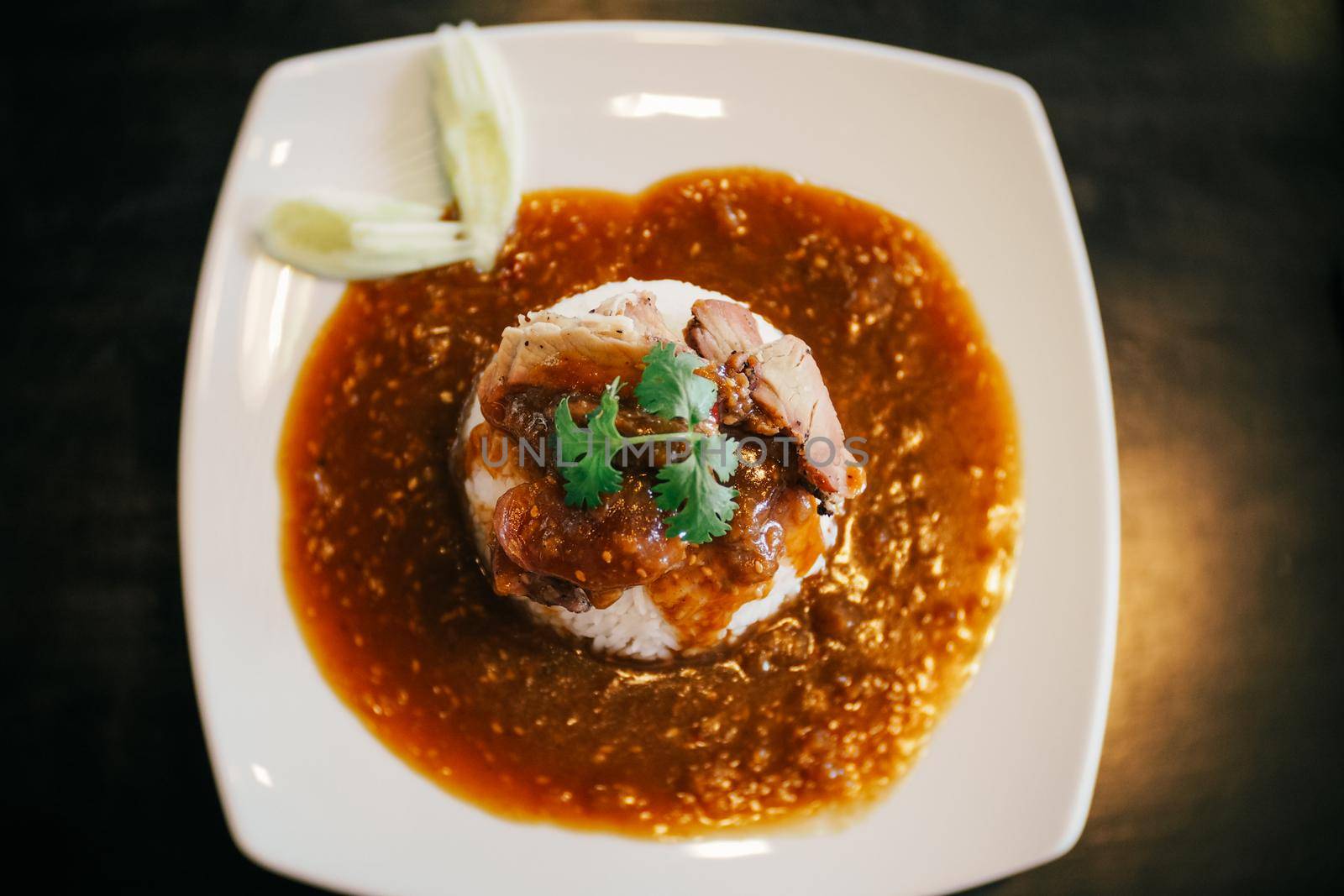 A plate of Chinese BBQ pork on rice with gravy on top.