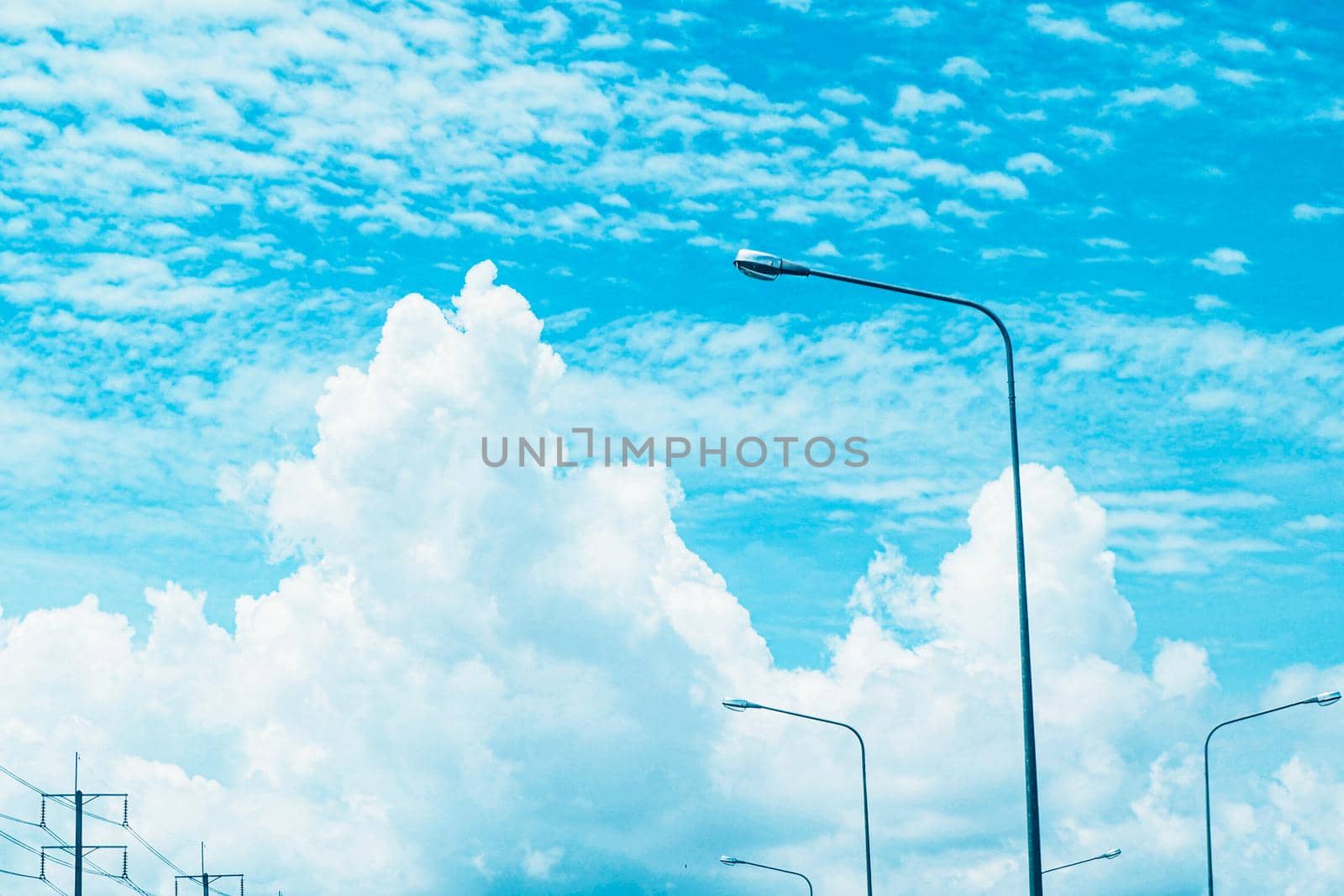 Electric lighting lamp against blue sky with white fluffy cloud.