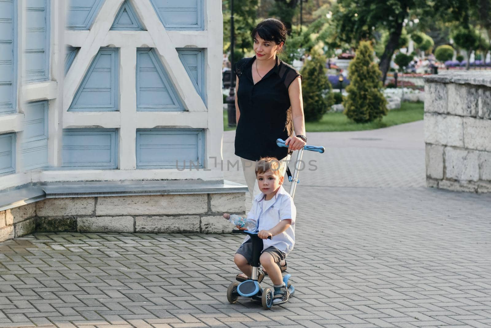 Mother with son riding scooters in summer by Godi