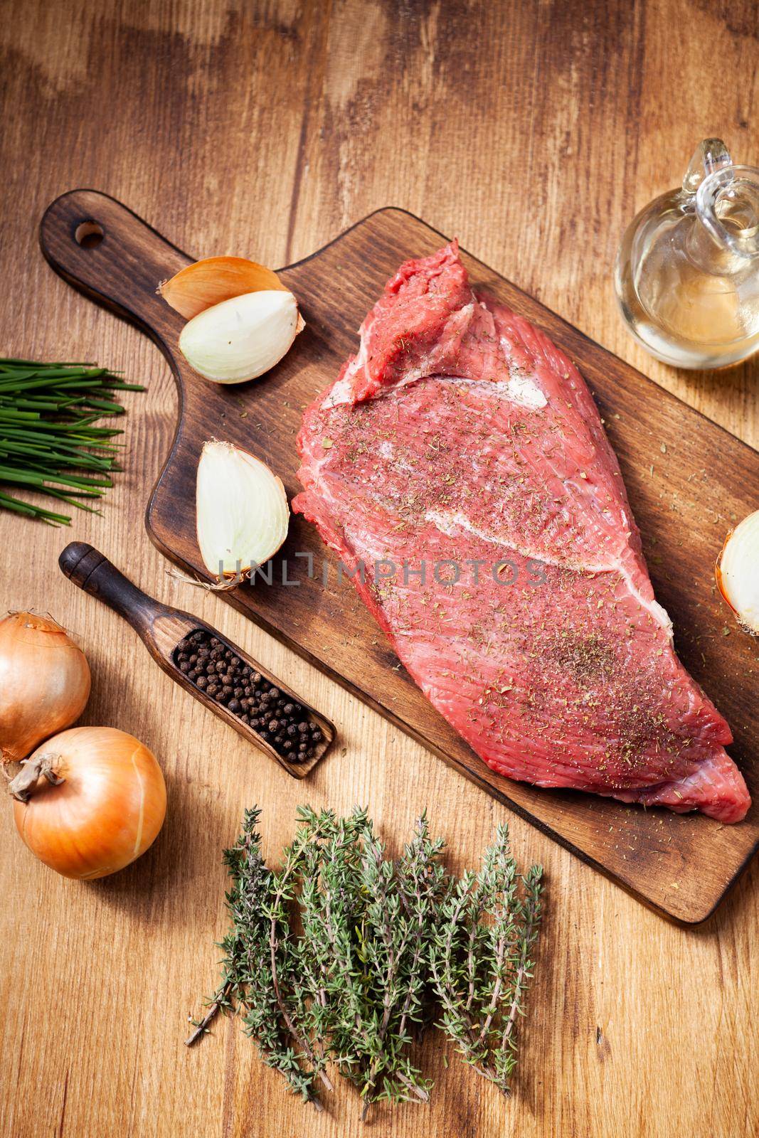 Raw beef steak on wooden cutting board next to onions and seasoned with rosemary. Meat preparation. Natural ingredients.