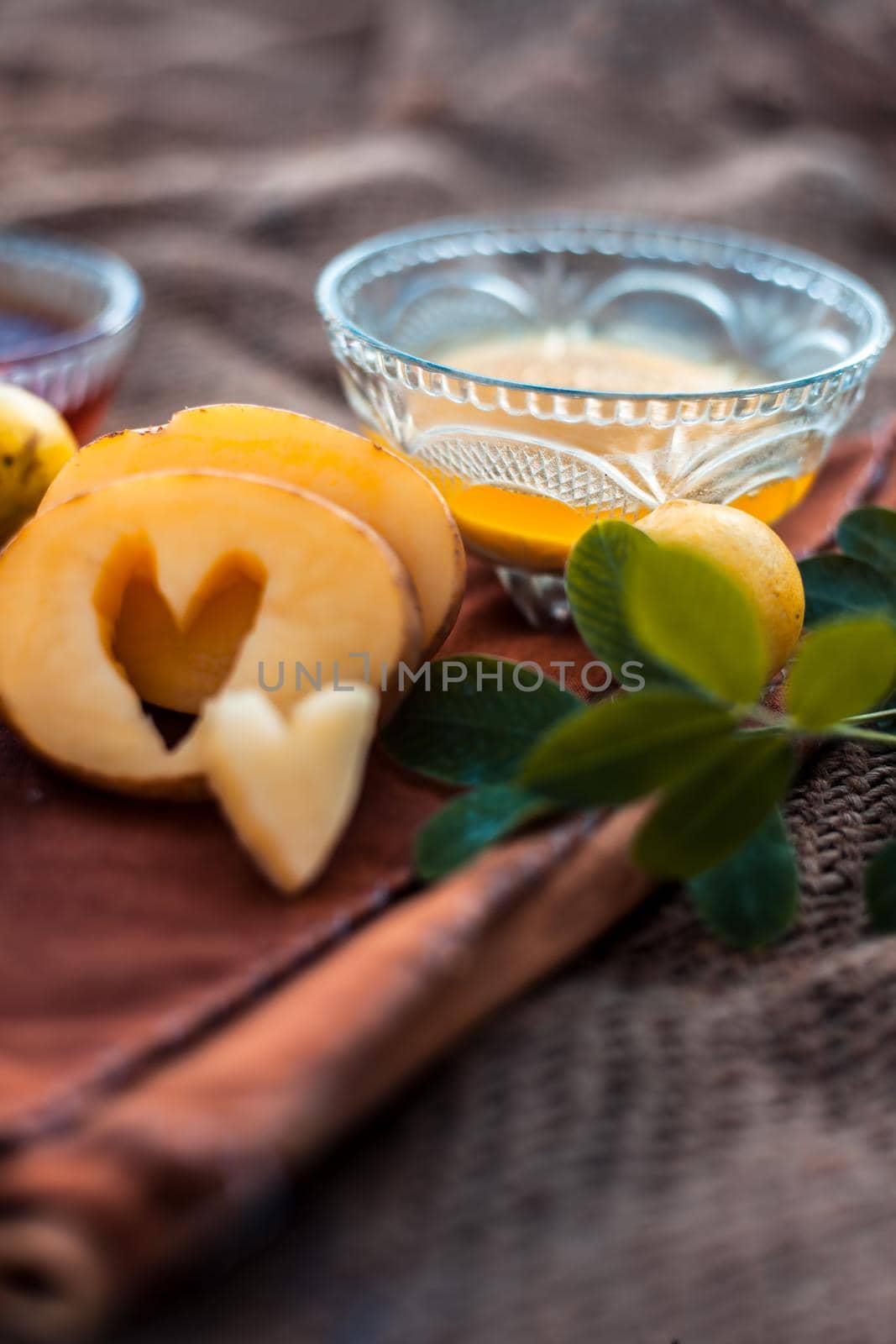 Glowing face mask of potato juice in a glass bowl on brown colored surface along with some lemon juice,potato juice and honey.Horizontal shot. by mirzamlk