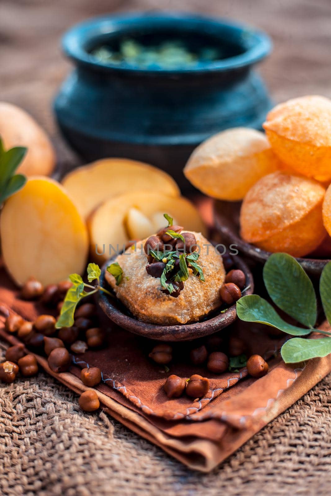Famous Indian & Asian street food dish i.e. Panipuri snack in a clay bowl along with its flavored spicy water in another clay vessel. Entire consisting raw ingredients present on the surface. by mirzamlk