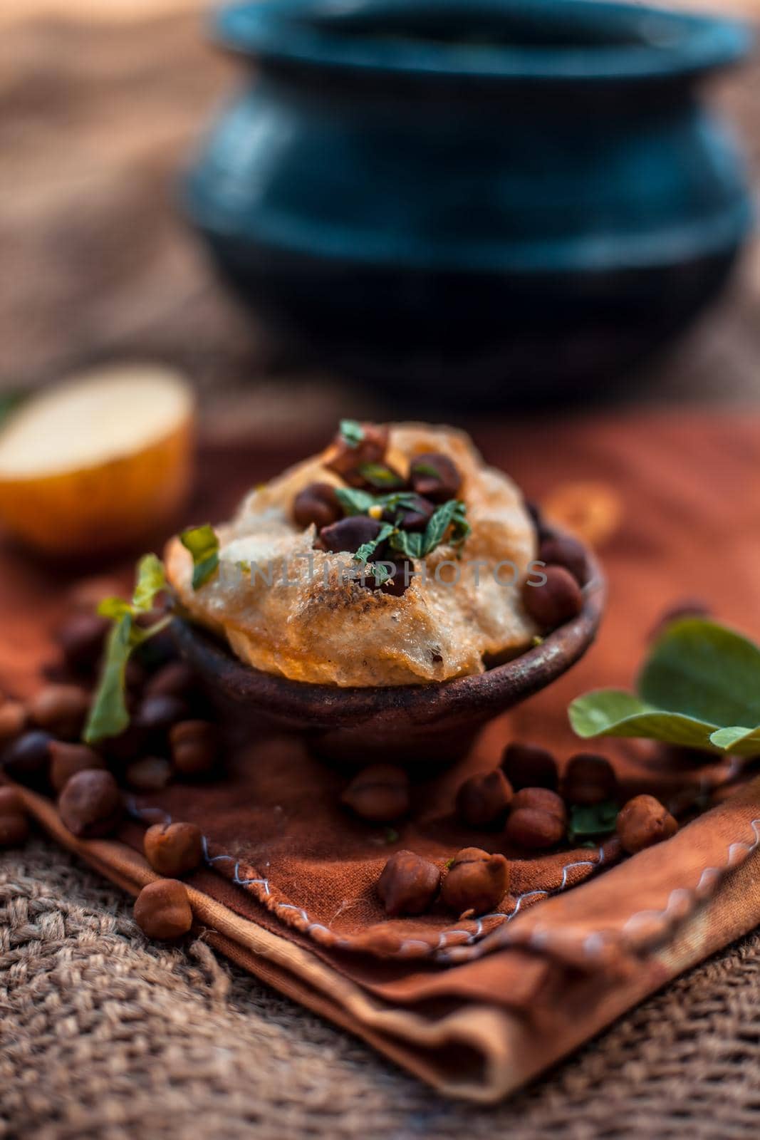 Famous Indian & Asian street food dish i.e. Golgappa snack in a clay bowl along with its flavored spicy water in another clay vessel. Vertical shot of the snack and its ingredients present.