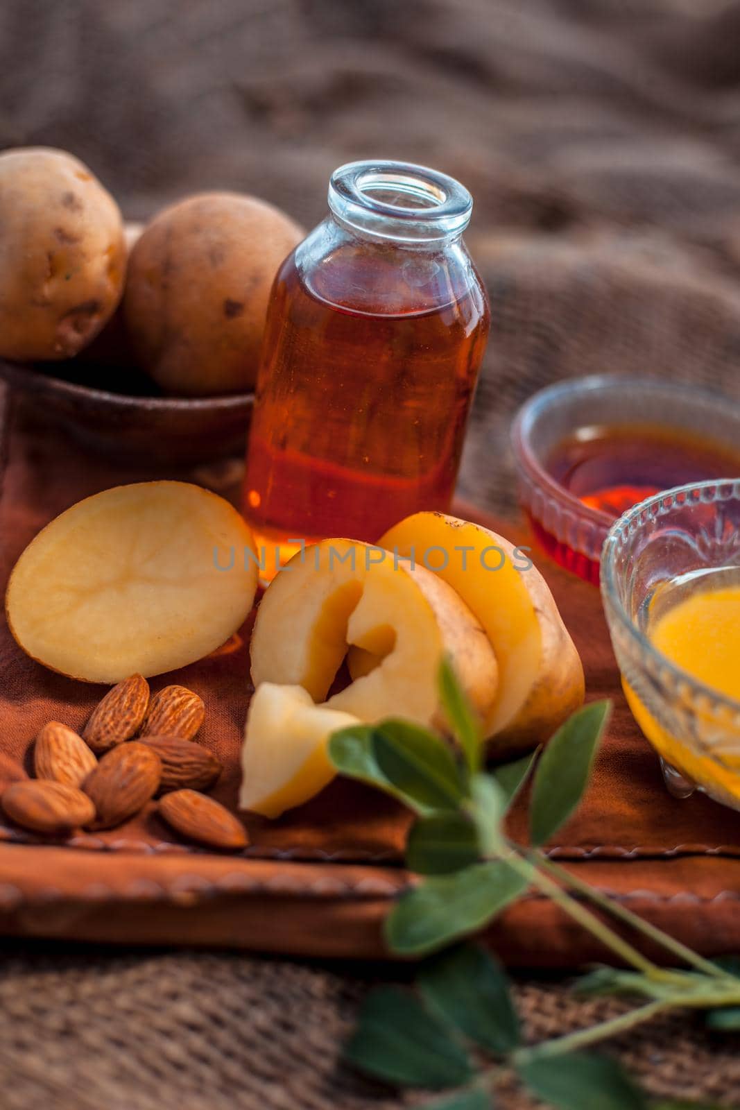 Glowing face mask of potato juice in a glass bowl on brown colored surface along with some Potato juice,honey and almond oil.Horizontal shot.To eliminate skin rashes, remove impurities,etc.