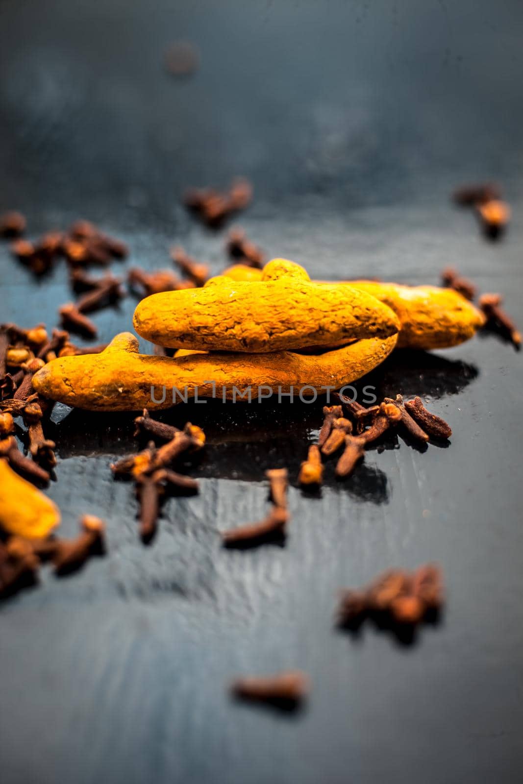 Face mask or pack’s ingredients on wooden surface for acne which are turmeric or haldi and cloves. Ingredients spread on the surface. Vertical shot. by mirzamlk