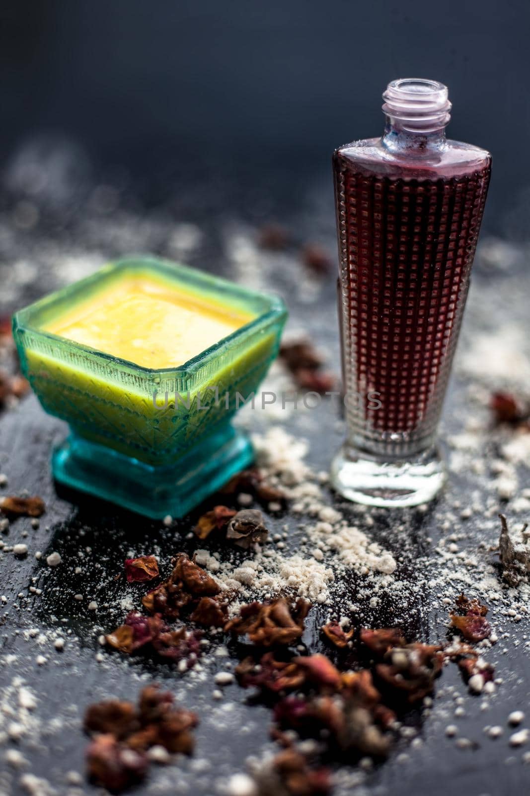 Face mask for skin whitening on wooden surface consisting of besan or gram flour and some rose water. With some dried rose petals and gram flour spread on the surface. Vertical shot.