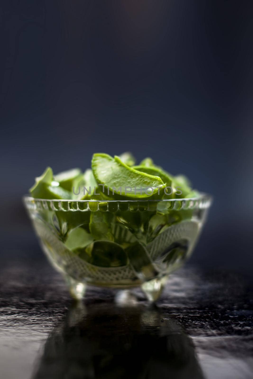 Raw cut aloevera or aloe vera gel in a glass bowl on wooden surface along with its reflection on the surface.