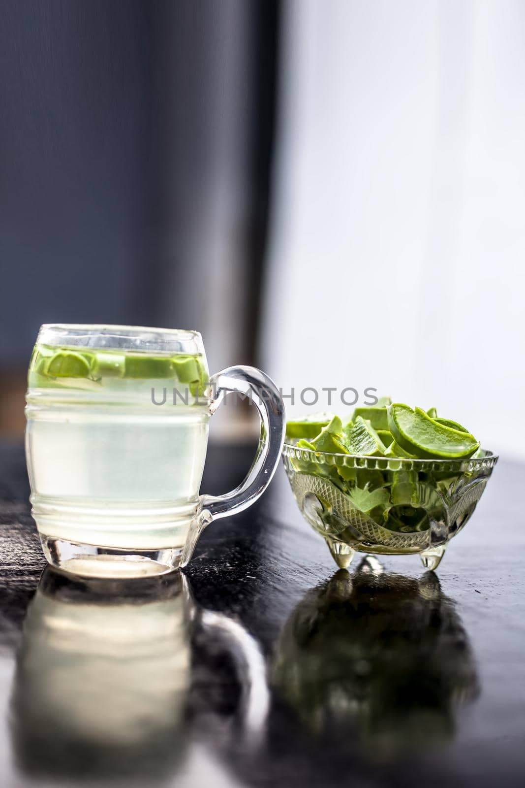Close up of glass mug on wooden surface containing aloe vera detox drink in along with its entire raw ingredients with it. Vertical shot with blurred background.