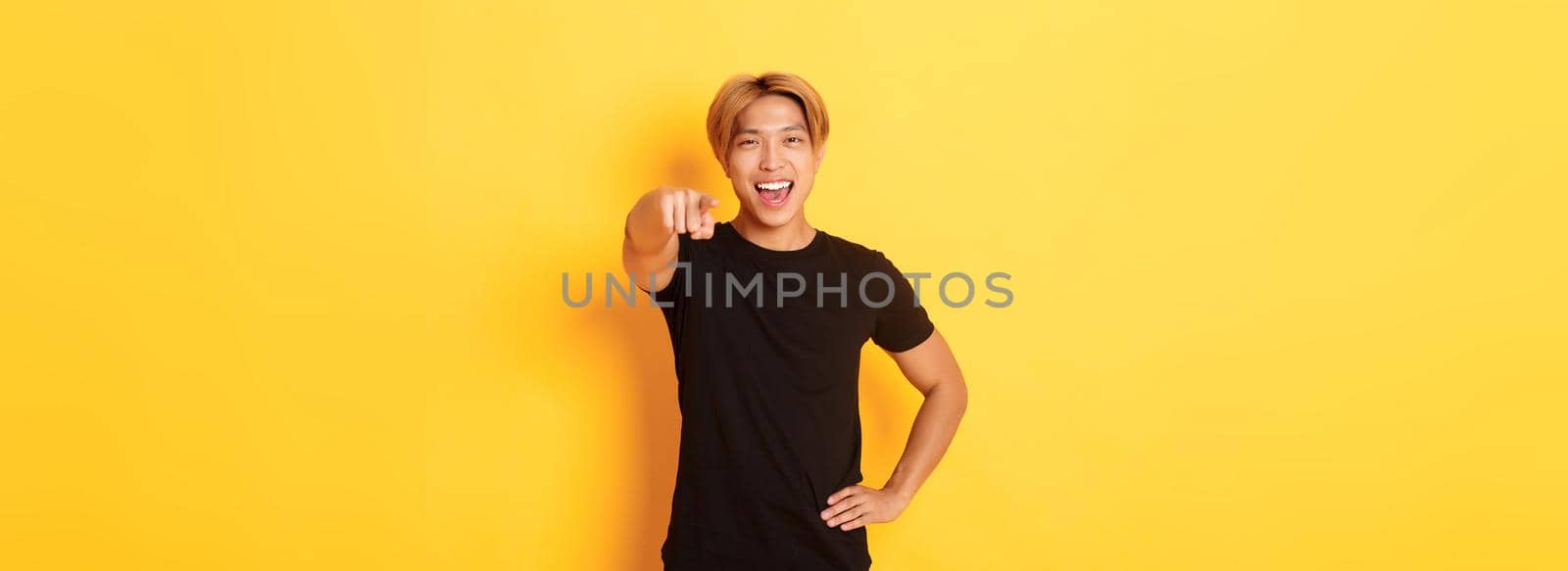 Portrait of cheerful handsome asian guy with blond hair choosing you, smiling and pointing finger at camera, congrats gesture by Benzoix