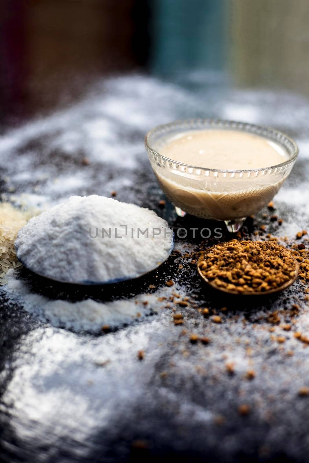 Hair growth remedy of rice flour water and fenugreek/coriander/parsley seeds powder on wooden surface and its paste in a glass bowl with some rice flour spread on the surface. Vertical shot.