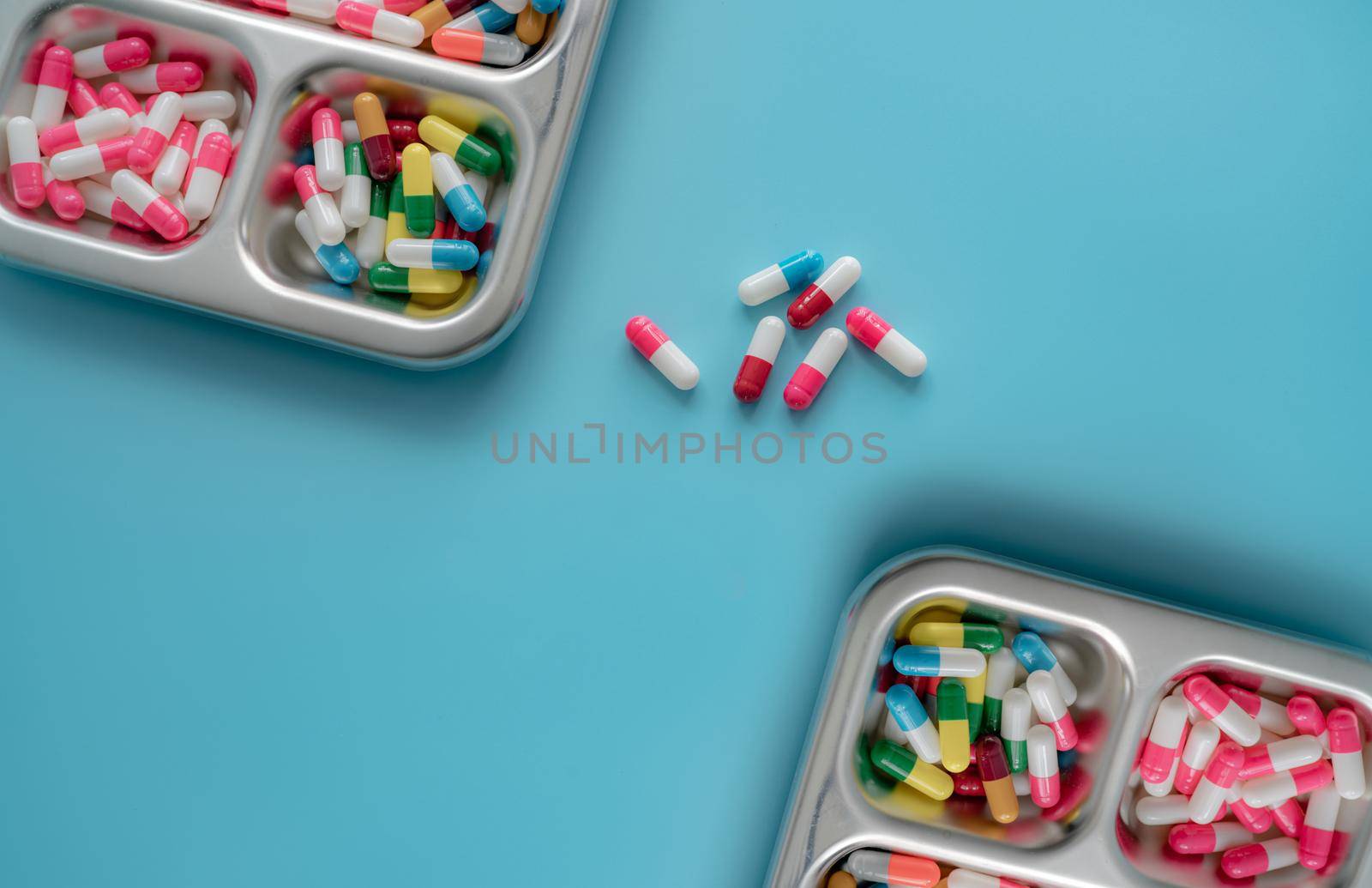 High angle view of multi-colored antibiotic capsule pills on stainless steel tray and blue background. Antibiotic drug resistance. Prescription drugs. Pharmaceutical industry. Capsule pill production.