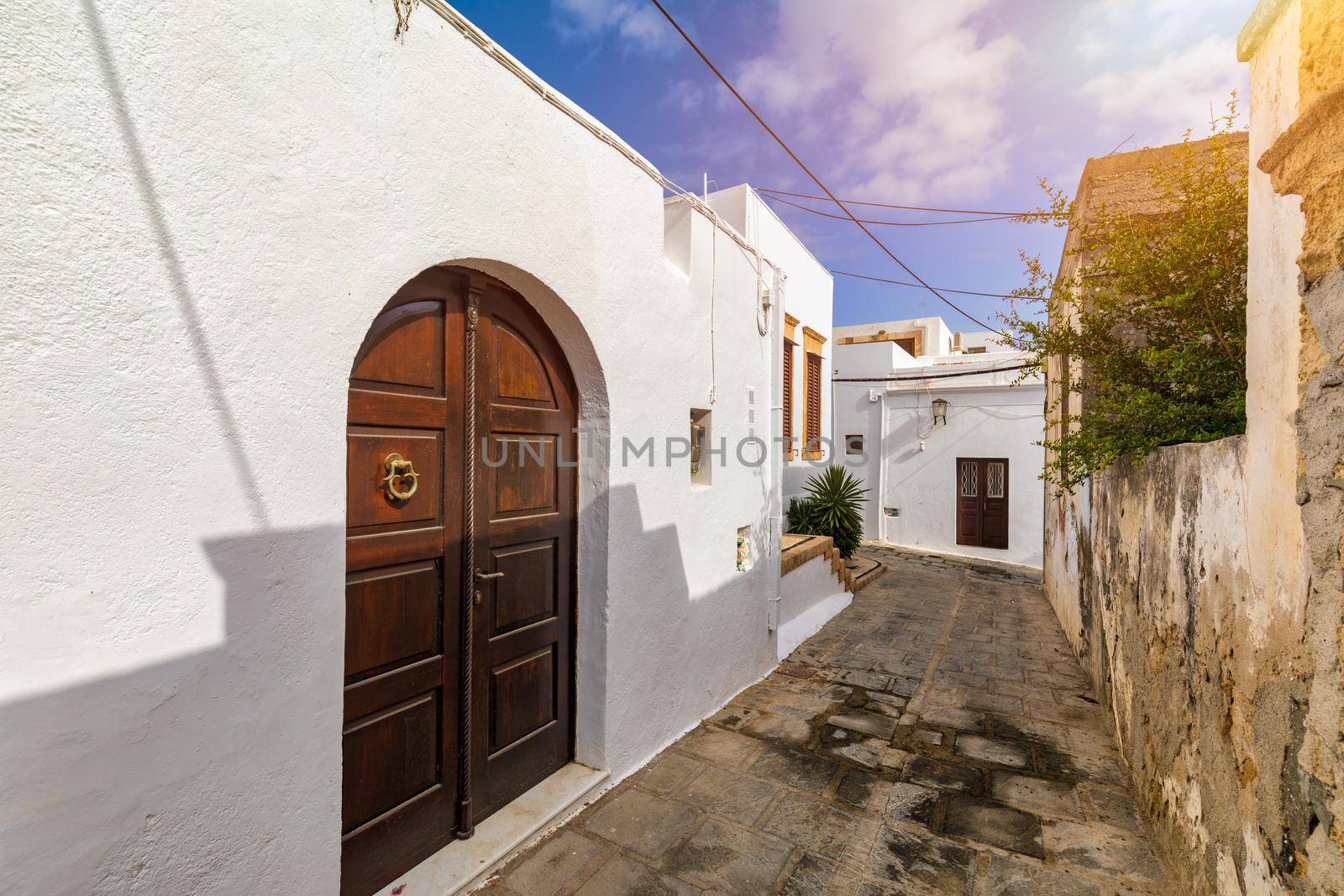 Narrow street in Lindos town on Rhodes island, Dodecanese, Greece. Beautiful scenic Lindos old ancient white houses with flowers. Famous tourist destination in South Europe. Lindos, Rhodes, Greece.