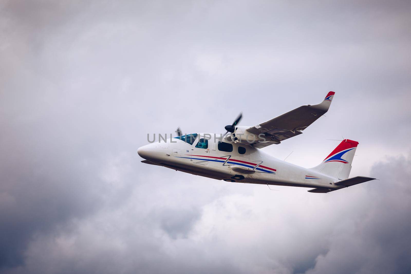 Light small plane flies against the background of white rainy clouds not high above the ground. Light aircraft on the air. A small tourist plane on an isolated white rainy clouds.