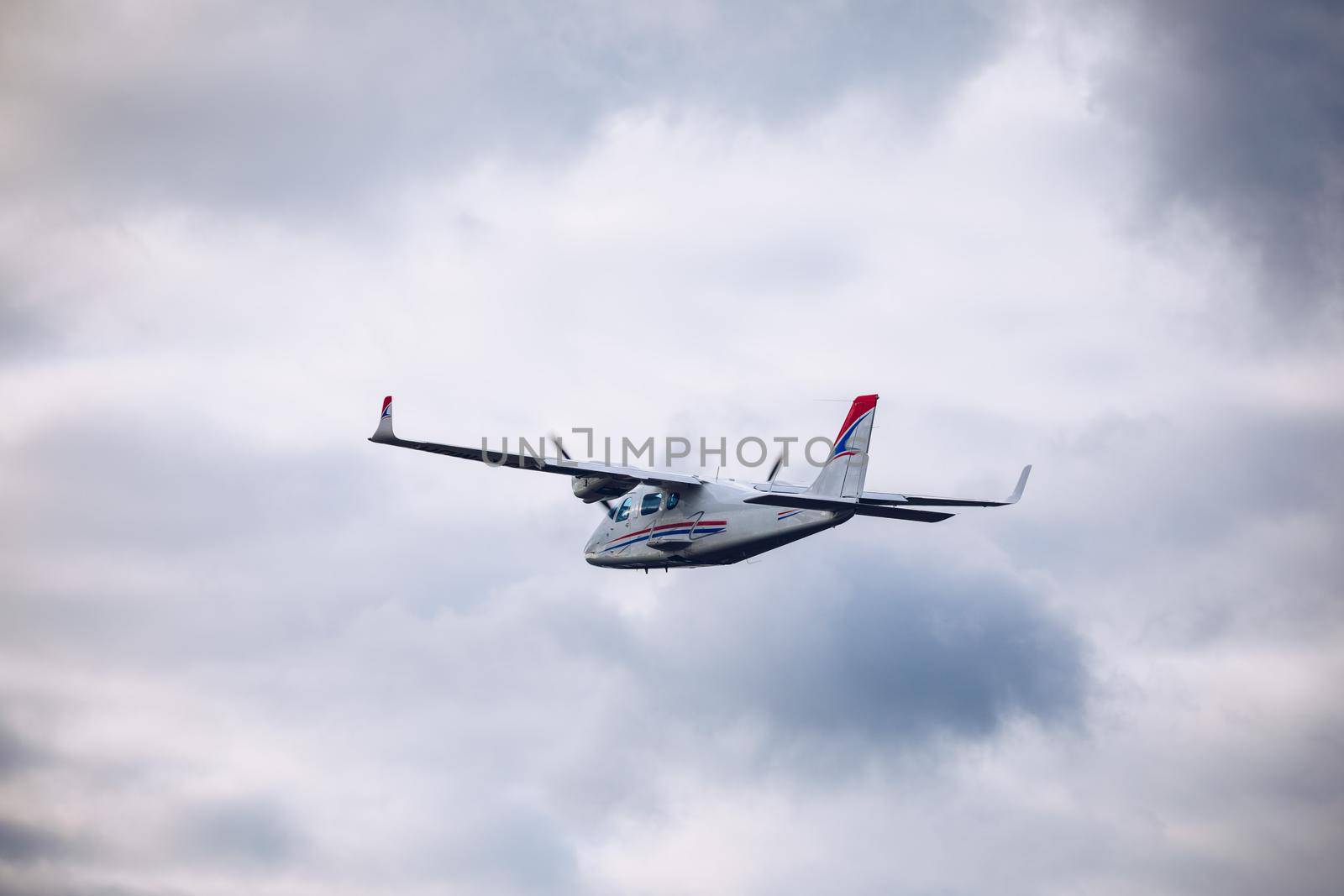 Light small plane flies against the background of white rainy clouds not high above the ground. Light aircraft on the air. A small tourist plane on an isolated white rainy clouds.