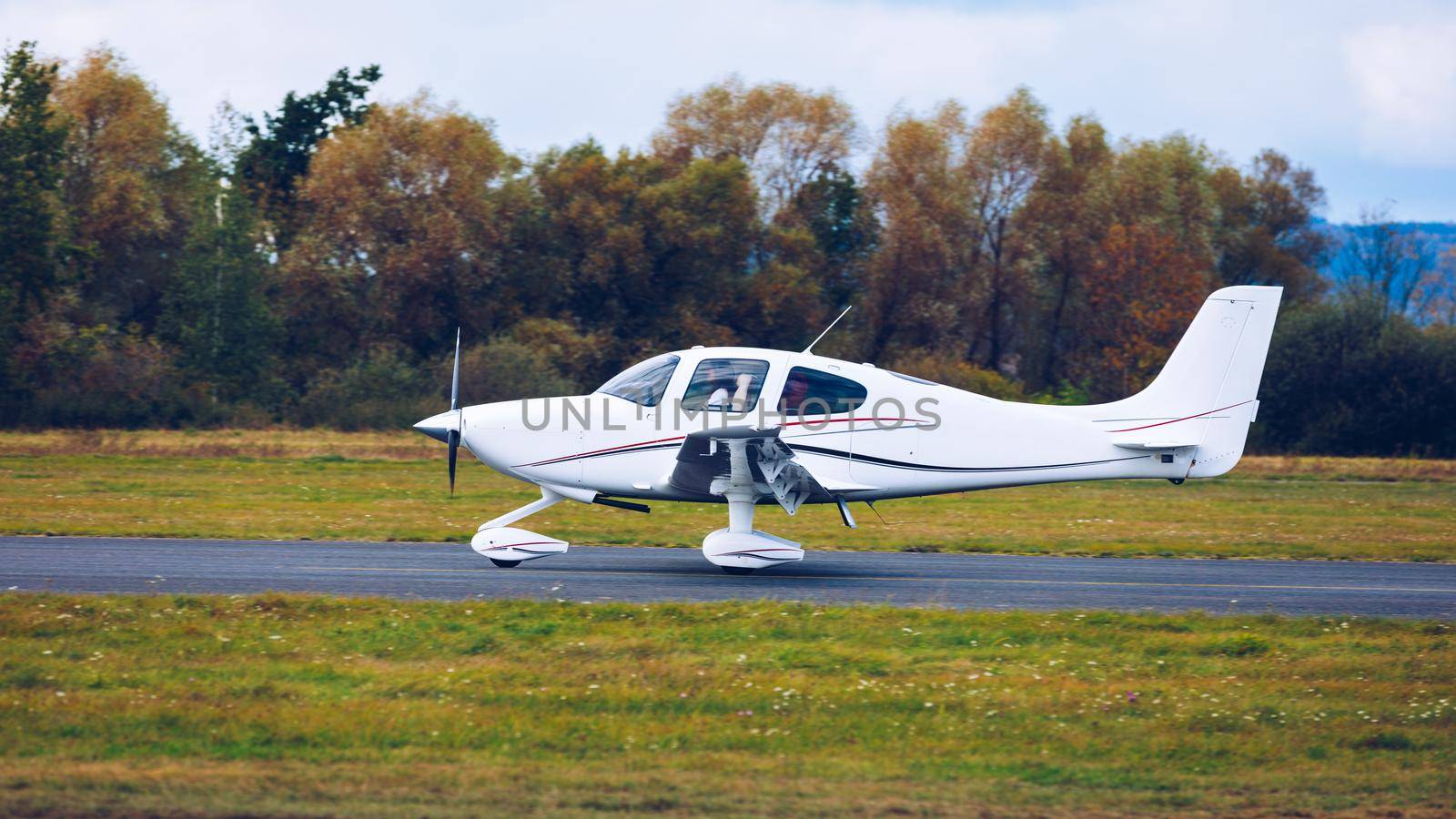 Light small plane flies against the background of a forest not high above the ground. Light aircraft on the air. A small tourist plane on an isolated white rainy clouds.