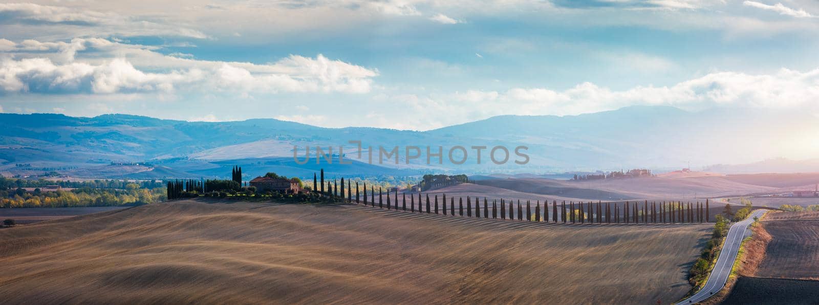 Well known Tuscany landscape with grain fields, cypress trees and houses on the hills at sunset. Summer rural landscape with curved road in Tuscany, Italy, Europe