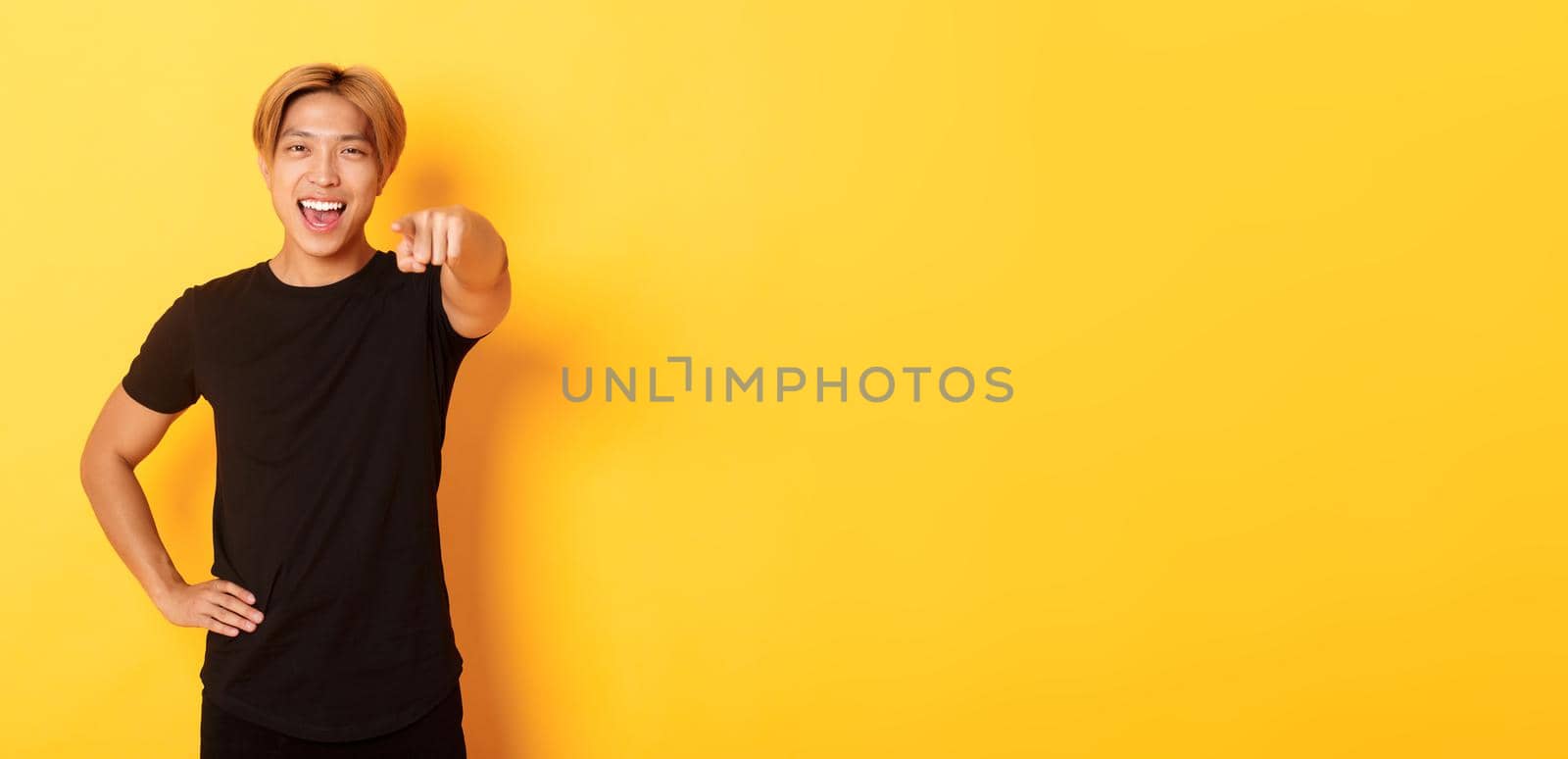 Portrait of cheerful handsome asian guy with blond hair choosing you, smiling and pointing finger at camera, congrats gesture.