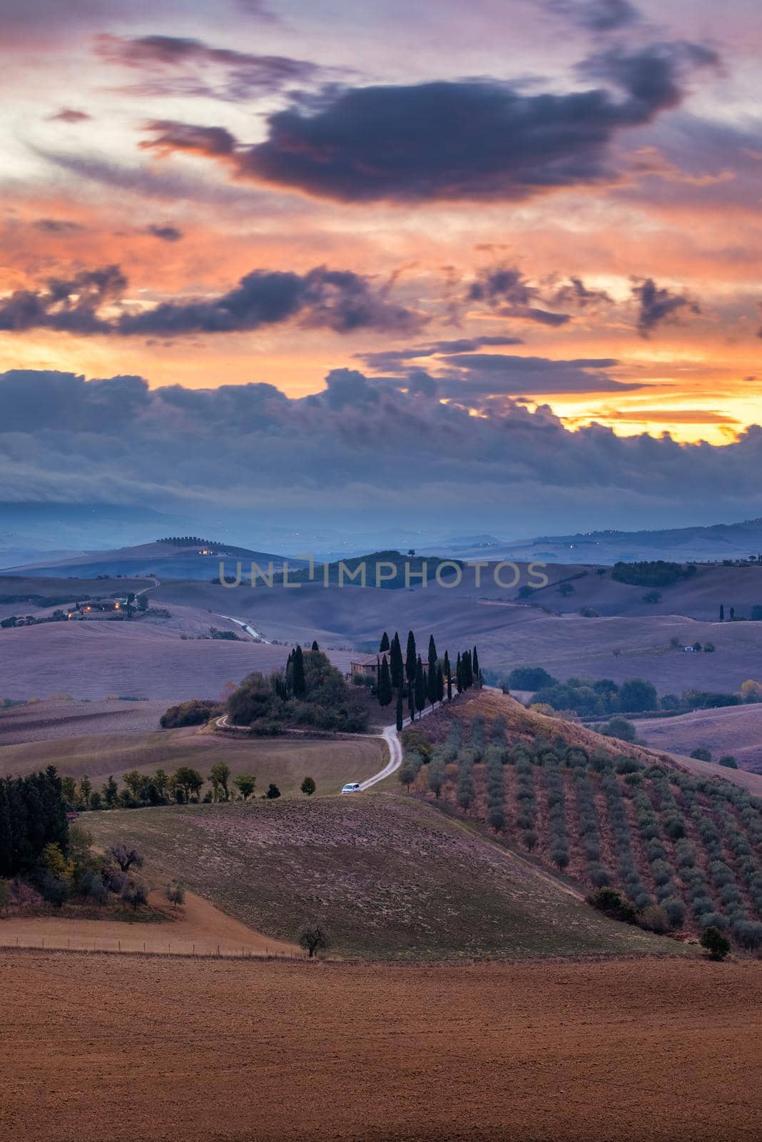 Well known Tuscany landscape with grain fields, cypress trees and houses on the hills at sunset. Summer rural landscape with curved road in Tuscany, Italy, Europe
