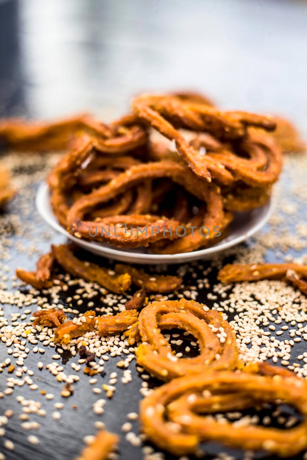 Famous Indian snack in a glass plate on the wooden surface along with raw sesame seeds or til spread on the surface.