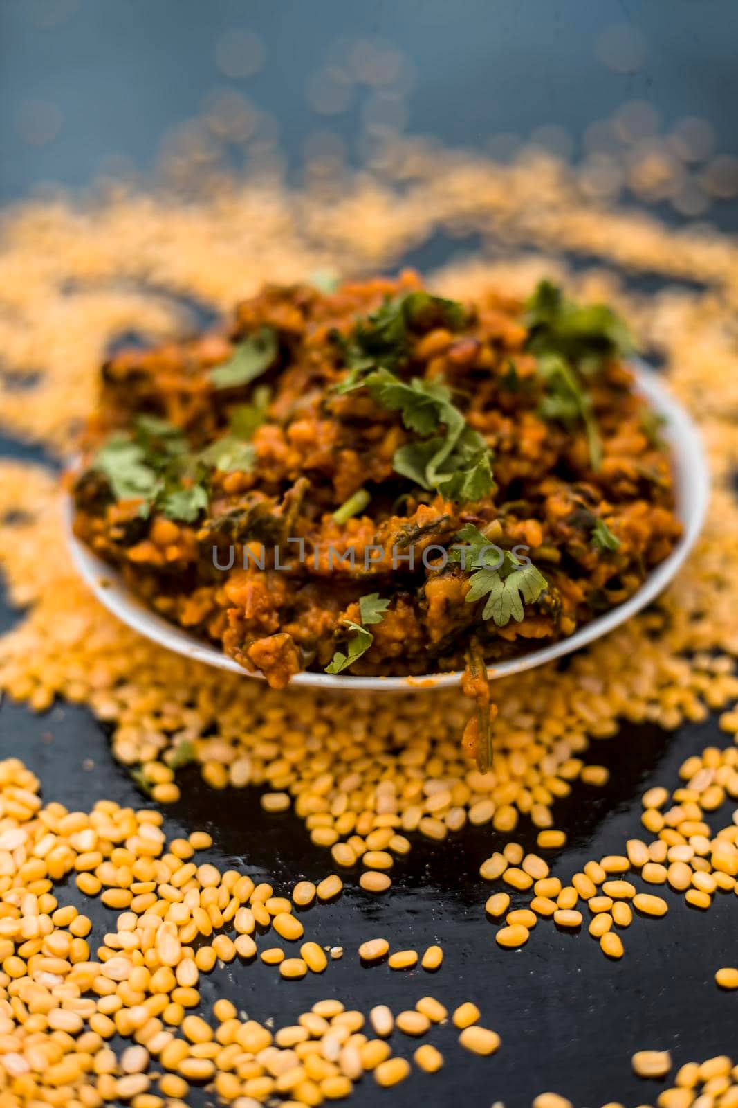 Famous Indian Punjabi dish i.e. Roasted dal with spinach in a glass plate on the wooden surface along with its main ingredients i.e. Unskinned split moong dal.