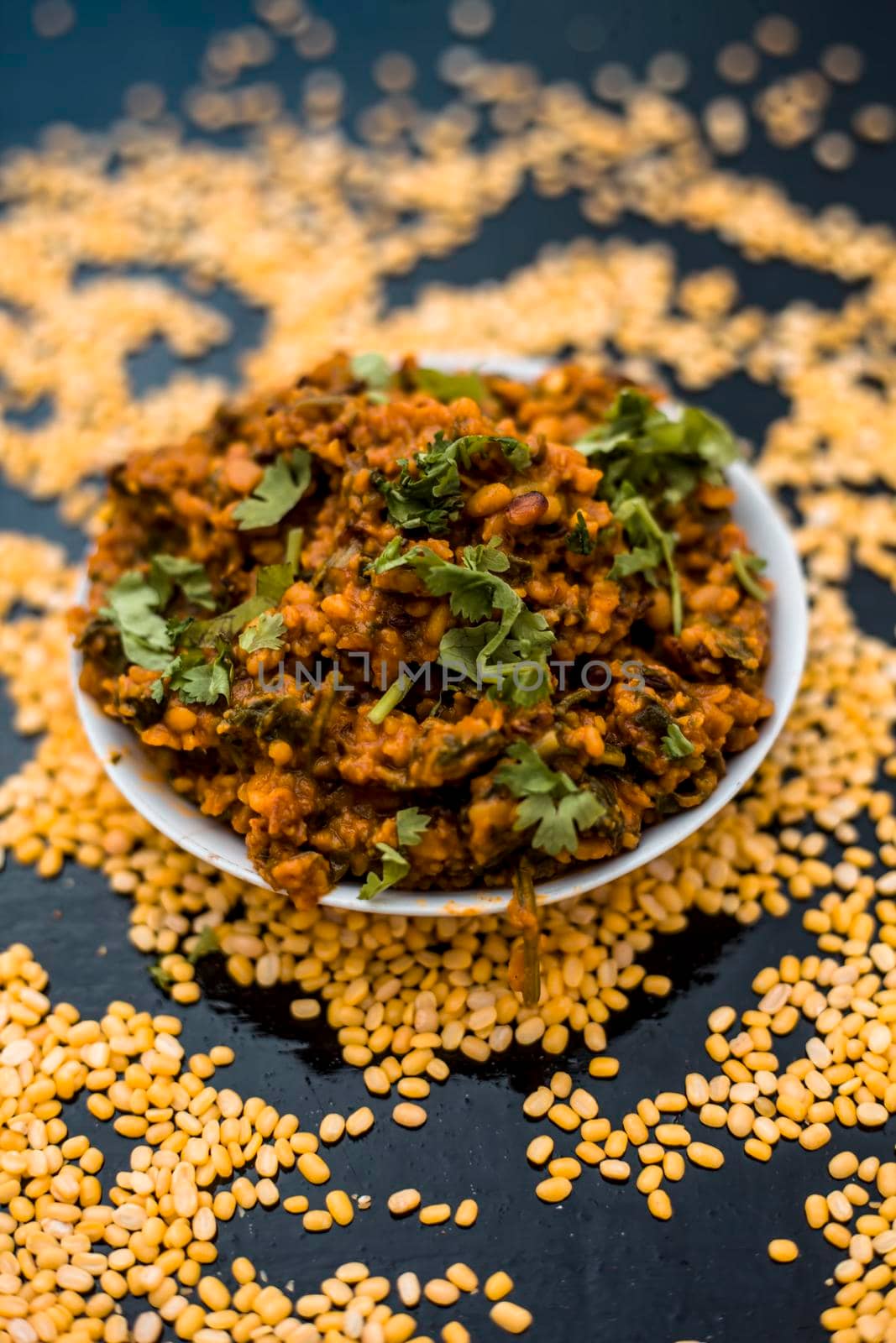 Famous Indian Punjabi dish i.e. Roasted dal with spinach in a glass plate on the wooden surface along with its main ingredients i.e. Unskinned split moong dal. by mirzamlk