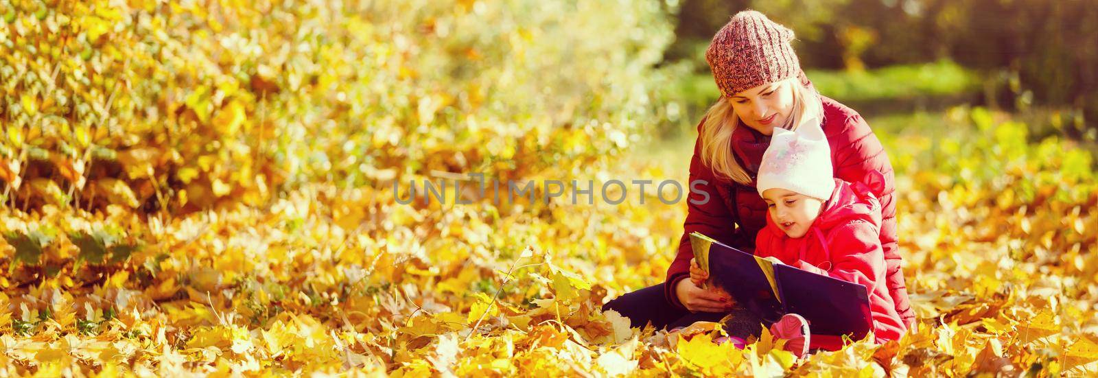 mother teaching daughter in autumn park, Mother teaching daughter to read.