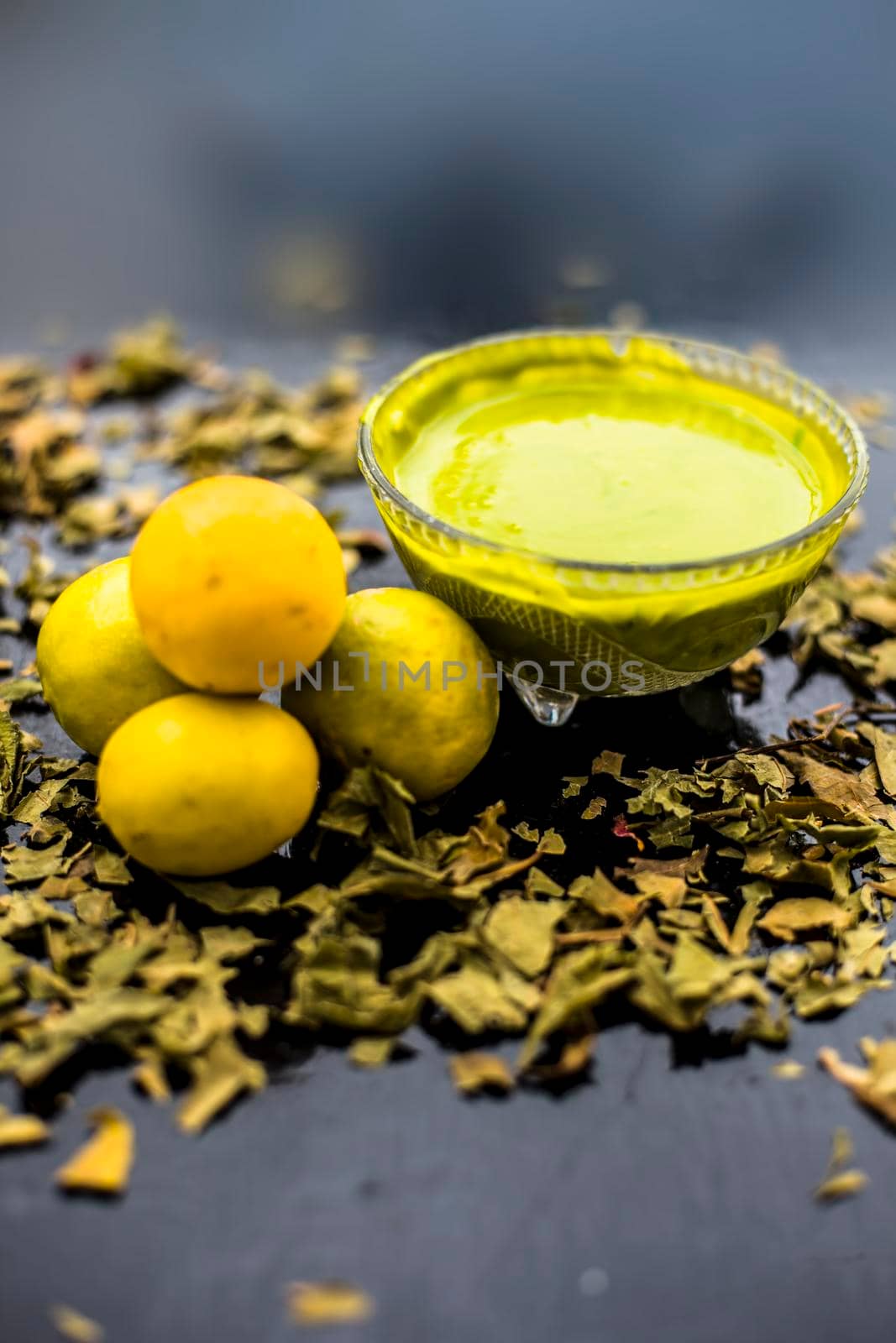Neem or Indian Lilac face mask on the black wooden surface for oily skin consisting of neem leaves paste and lemon juice well mixed with rose water.