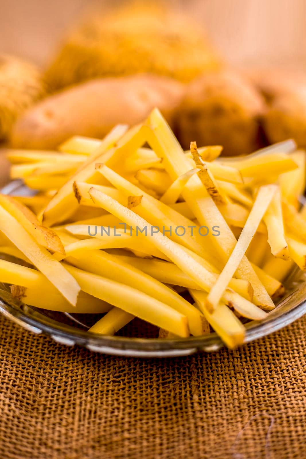 Raw cut french fries in a transparent glass plate along with raw potato with it on jute bag's surface. by mirzamlk