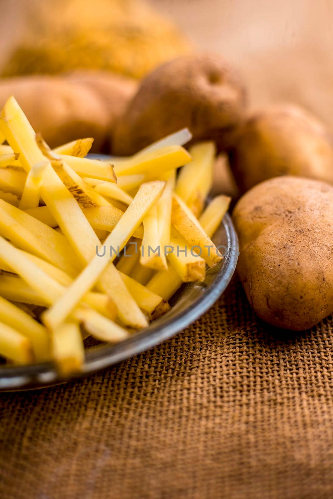 Raw cut french fries in a transparent glass plate along with raw potato with it on jute bag's surface. by mirzamlk