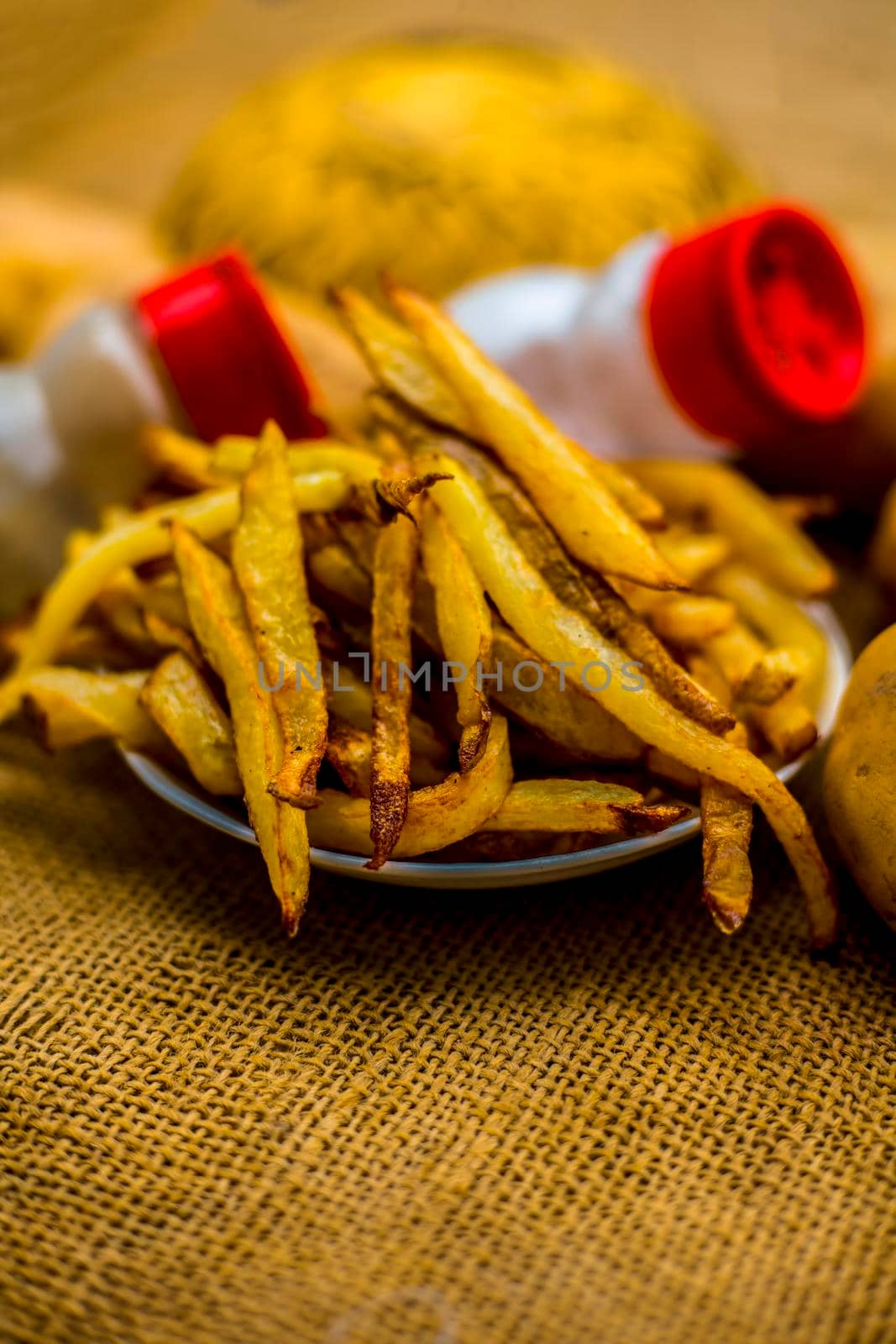 Fresh fired French fries of along with sprinkler of black pepper and salt on jute bag's surface and some raw potato also.