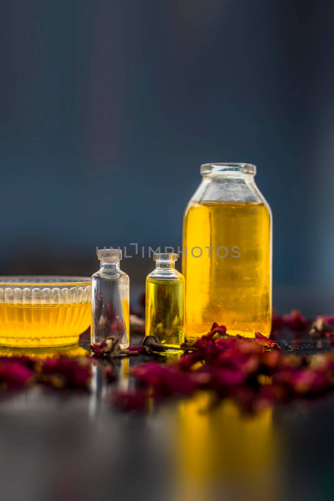 Close up of castor oil, tea tree oil, and some coconut oil in bottles on the wooden surface along with some raw honey and rose petals also present on the surface. by mirzamlk
