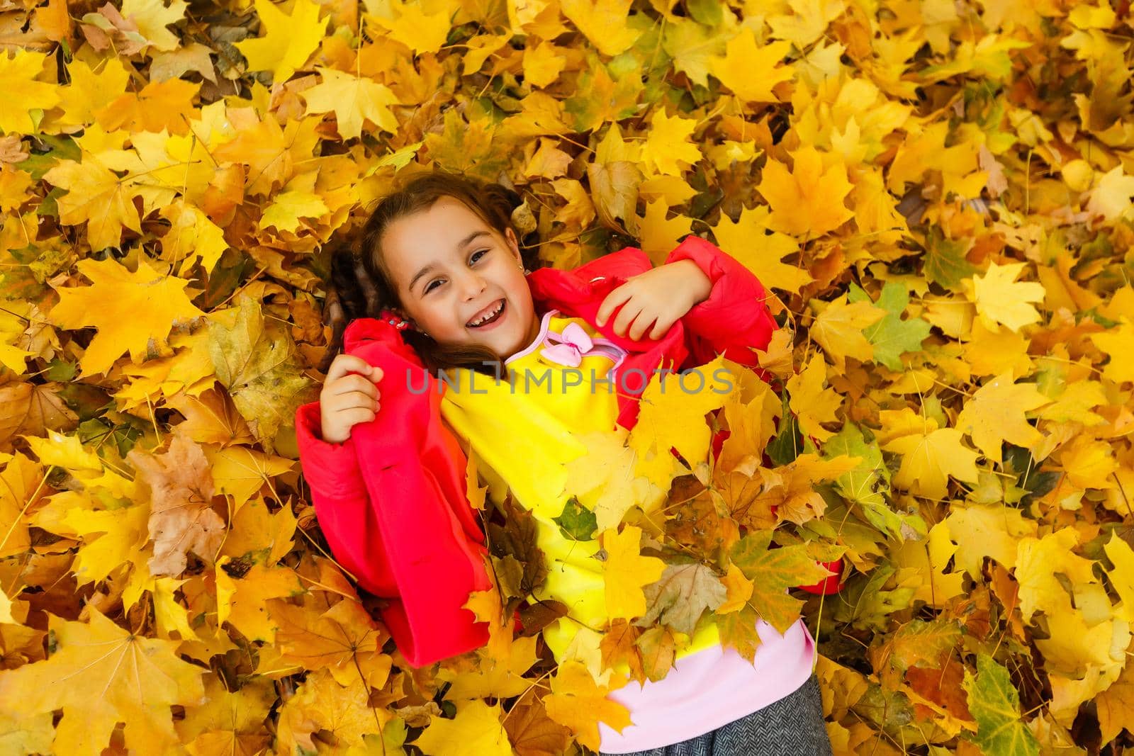 Happy little girl lies in yellow leaves in autumn park